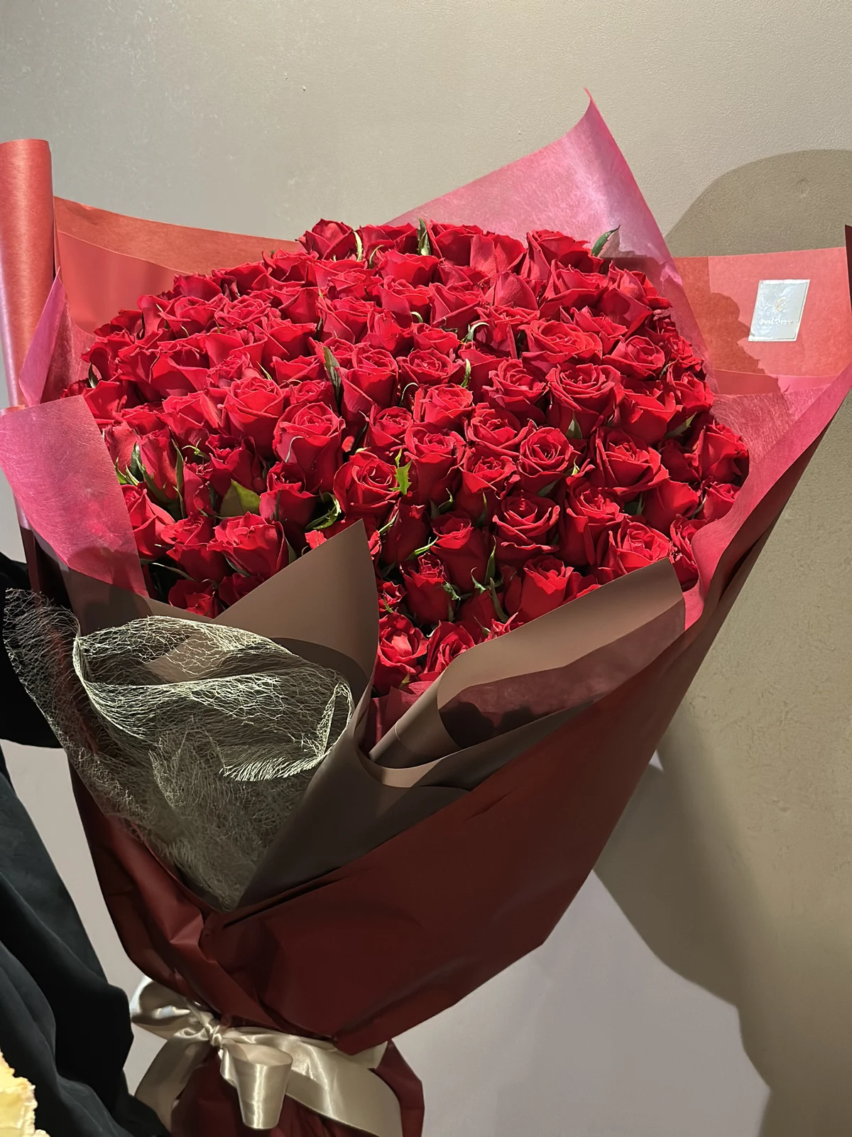 丸く整えたたくさんの赤薔薇を、ボルドーの包装とゴールドのリボンで仕上げた花束